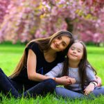 Happy beautiful young woman with girl in blossom park with trees and flowers.